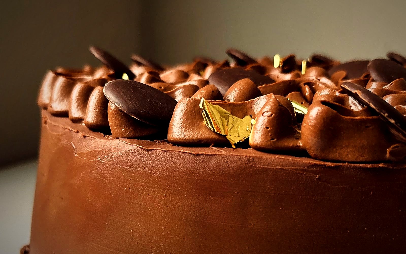 A lateral do Bolo de Café: a borda de ganache com discos de chocolate e uma folha de ouro